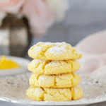 Lemon Cake Mix Cookies: Easy, Soft, and Delicious! 15 Stack of soft, yellow lemon cake mix cookies dusted with powdered sugar, arranged on a white plate with a blurred floral background.
