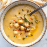 Top view of a bowl full of vegan garlic chickpea soup with a spoon served with crusty bread.