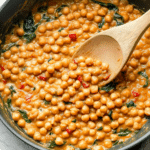 Marry Me Chickpeas: A Creamy Vegan Delight! 15 a wooden spoon stirring a batch of Marry Me Chickpeas in a large skillet.